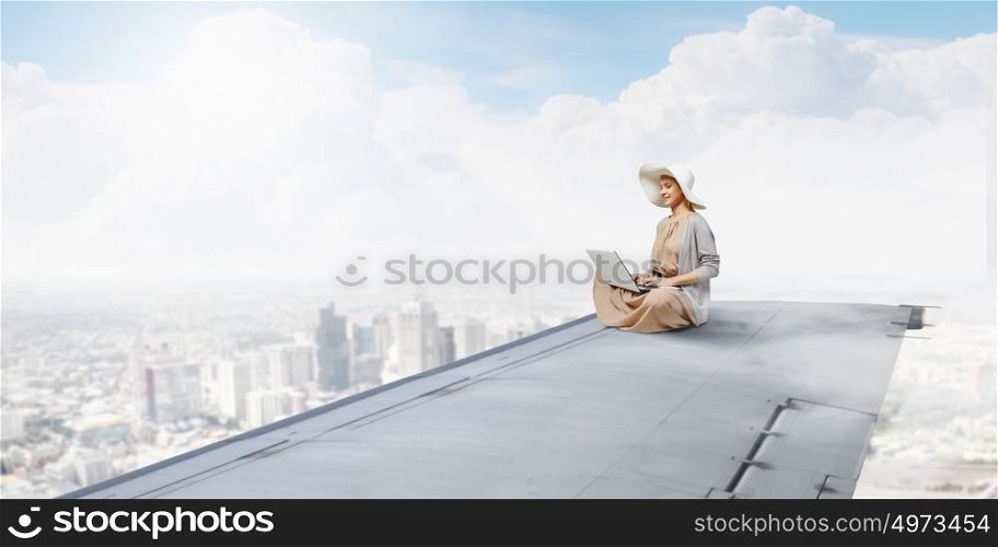 Writer woman working in isolation. Woman in dress and hat sitting on airplane wing and working on laptop