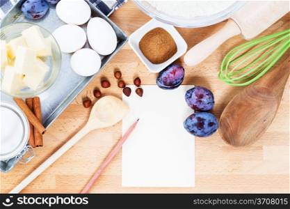 writing a recipe for plum cake. writing a recipe for plum cake with baking ingredients and tools from top with paper and a pencil