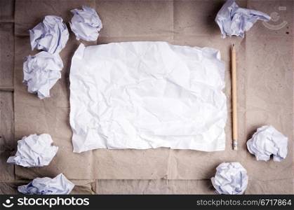 Writing concept - crumpled up paper wads with a sheet of white paper and pencil