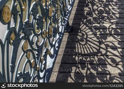Wrought iron decorative fence on bridge. Forming an interesting design with it&rsquo;s cast shadow on the floor. Selective focus.