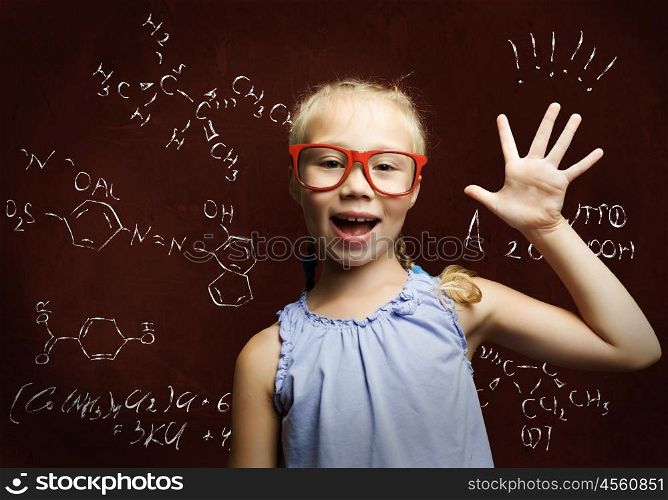 Wunderkind. Cute school girl in glasses standing at blackboard