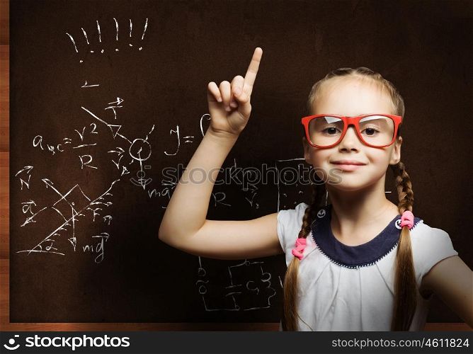 Wunderkind. Cute school girl in glasses standing at blackboard