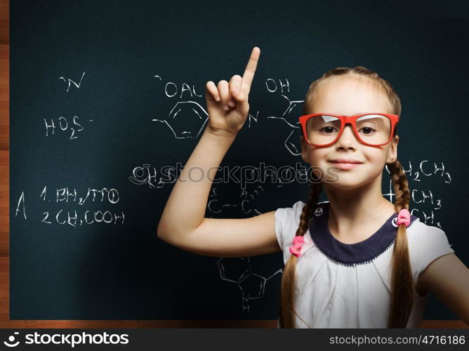 Wunderkind. Cute school girl in glasses standing at blackboard