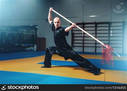 Wushu master training with spear, martial arts. Man in black cloth poses with blade
