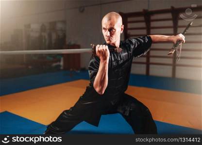 Wushu master training with sword, martial arts. Man in black cloth poses with blade. Wushu master training with sword, martial arts