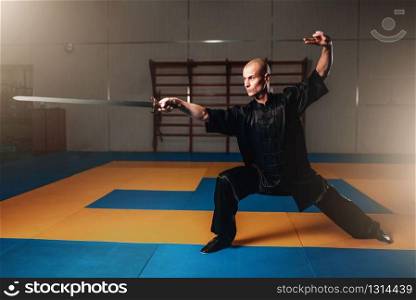 Wushu master training with sword, martial arts. Man in black cloth poses with blade. Wushu master training with sword, martial arts