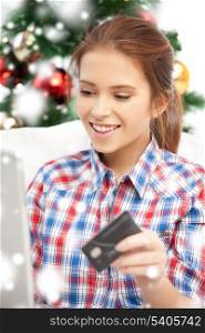 x-mas, christmas, online shopping and happiness concept - happy woman with laptop computer and credit card over christmas tree