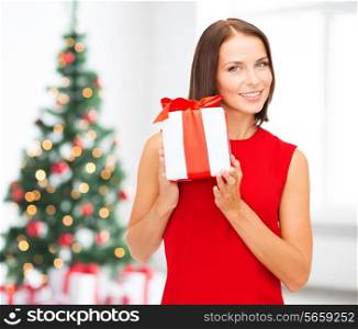 x-mas, holidays, valentine&#39;s day, celebration and people concept - smiling woman in red dress with gift box over living room and christmas tree background