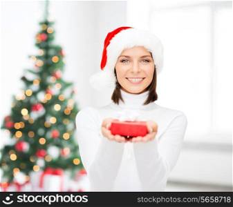 x-mas, winter, happiness, holidays and people concept - smiling woman in santa helper hat with small red gift box over living room and christmas tree background