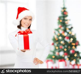 x-mas, winter, happiness, holidays and people concept - smiling woman in santa helper hat with gift box over living room and christmas tree background