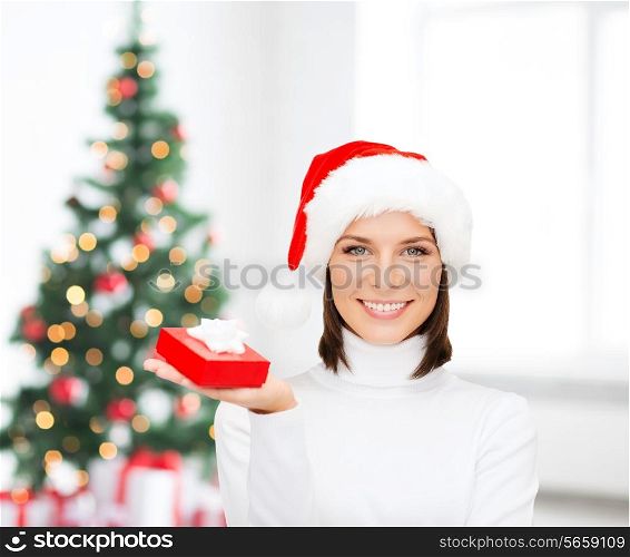 x-mas, winter, happiness, holidays and people concept - smiling woman in santa helper hat with small red gift box over living room and christmas tree background