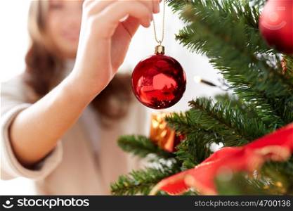 x-mas, winter holidays and people concept - happy young woman decorating christmas tree with ball at home