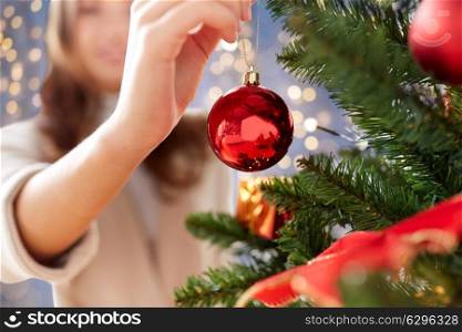 x-mas, winter holidays and people concept - happy young woman decorating christmas tree with ball at home. happy young woman decorating christmas tree