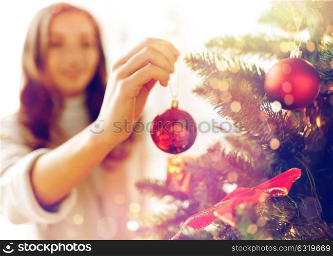 x-mas, winter holidays and people concept - happy young woman decorating christmas tree with ball at home. happy young woman decorating christmas tree