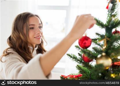 x-mas, winter holidays and people concept - happy young woman decorating christmas tree at home