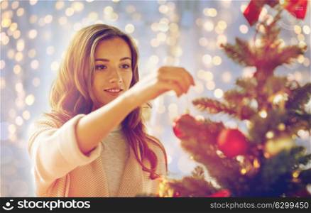 x-mas, winter holidays and people concept - happy young woman decorating christmas tree at home. happy young woman decorating christmas tree