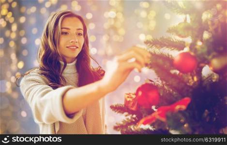 x-mas, winter holidays and people concept - happy young woman decorating christmas tree at home. happy young woman decorating christmas tree