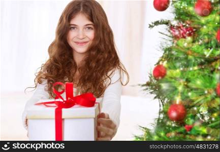 &#xA;Portrait of cute happy teen girl with gift box standing near beautiful decorated Christmas tree, with pleasure celebrating winter holidays