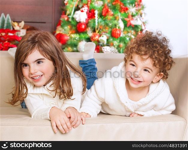 &#xA;Portrait of cute little brother and sister having fun at home, spending happy winter holidays, with pleasure playing games on the sofa near Christmas tree