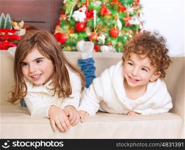 &#xA;Portrait of cute little brother and sister having fun at home, spending happy winter holidays, with pleasure playing games on the sofa near Christmas tree