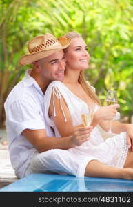 &#xA;Two people in love sitting near swimming pool on the beach resort and drinking champagne, romantic honeymoon vacation
