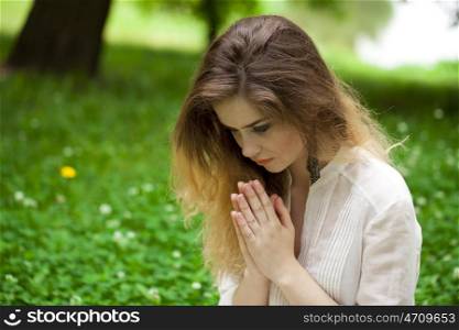 &#xA;Young beautiful girl praying sitting on the green lawn in the summer park