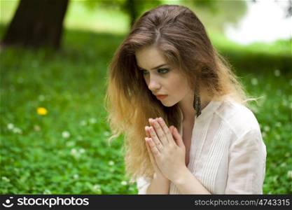 &#xA;Young beautiful girl praying sitting on the green lawn in the summer park