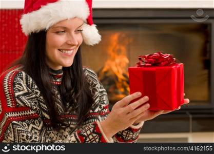 Xmas present happy woman by home fireplace wear Santa hat