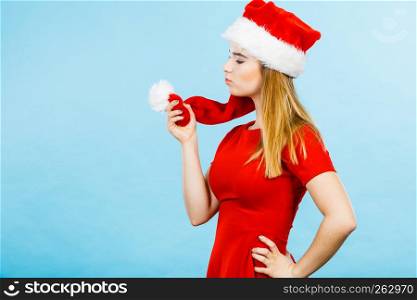 Xmas, seasonal clothing, winter christmas concept. Young smiling positive woman wearing Santa Claus helper costume playing with hat pompon. Woman wearing Santa Claus helper costume holding pompon