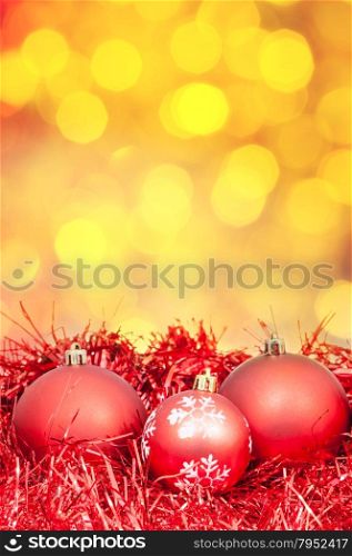 Xmas still life - red balls, tinsel with blurred yellow Christmas lights background