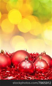 Xmas still life - red baubles, tinsel with blurred yellow and green Christmas lights bokeh background