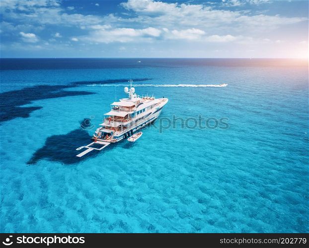 Yacht on the azure seashore in balearic islands. Aerial view of floating boat with people in transparent sea at sunset in summer. Top view from drone. Seascape with luxury yachts in bay. Travel