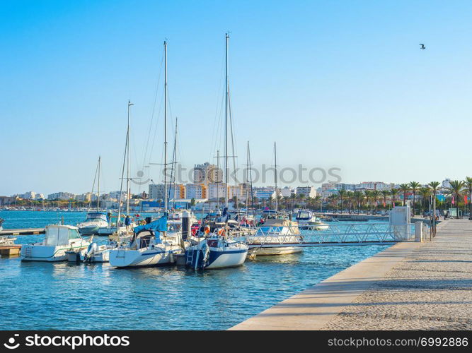 Yachts and motor boats moored in marina of Portimao, people walking at embankment in warm evening sunlight, Portugal, Europe