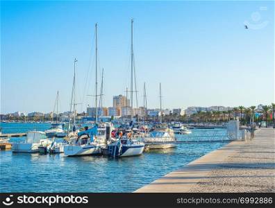 Yachts and motor boats moored in marina of Portimao, people walking at embankment in warm evening sunlight, Portugal, Europe