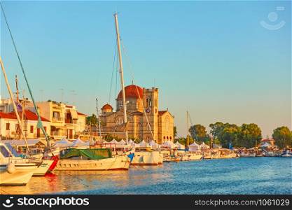 Yachts and waterfront with Ekklisia Isodia Theotokou Church at sunset in Aegina town, Saronic Islands, Greece