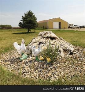 Yard art by farm building with rocks and chickens.