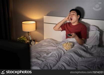 yawning sleepy man man watching TV movie on a bed at night