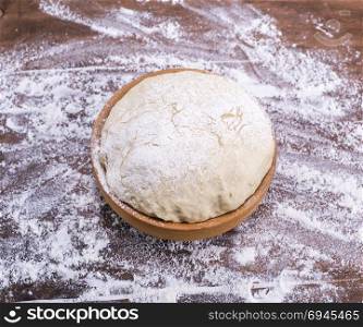 yeast dough made from white wheat flour in a wooden bowl on a brown table