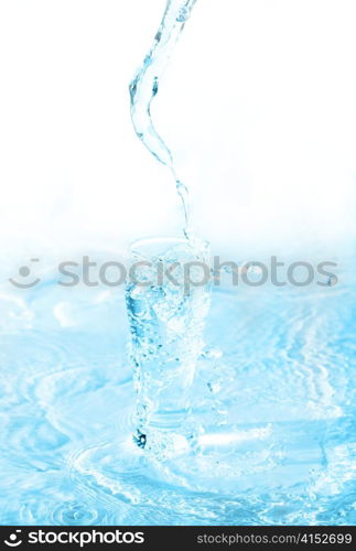 Yelllow drink being poured in a transparent glass with splashes on white