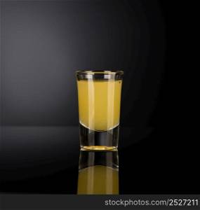 yellow alcoholic liquor in a shot glass isolated on dark background with backlight. shot glass with alcohol on a dark background
