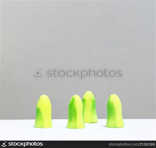 yellow and green ear plugs in a row, there are 4, in front of a white background.