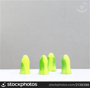 yellow and green ear plugs in a row, there are 4, in front of a white background.