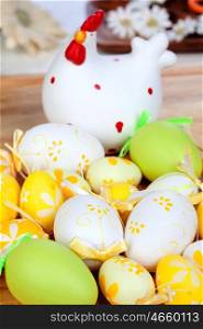 Yellow and green easter eggs with a ceramic hen on a wooden floor