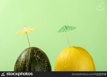 Yellow and green melons with cocktail umbrella on green background in sunlight. Summer drink concept. Different types of melon. Beverage ingredient.