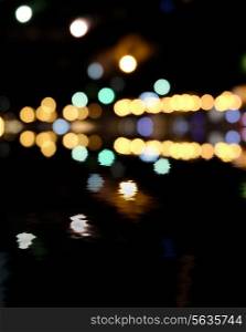 Yellow and green spots on black. Blurred city at night, bokeh background. Reflection of colorful lights in water and a lot of copyspace