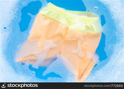 Yellow and orange baby shorts soak in baby laundry detergent water dissolution, washing cloth, blue background, Laundry concept.
