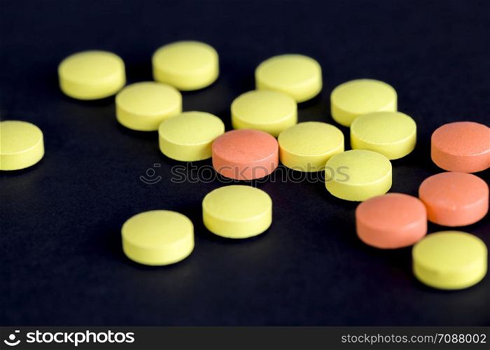 yellow and orange pills loose on a black background close-up of medical items. yellow and orange pills