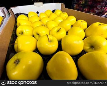 Yellow apples displayed in a cardboard box at the market.