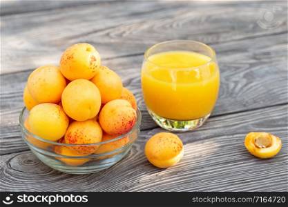 Yellow apricots in a glass bowl and juice on a wooden table. Yellow apricots in glass bowl and juice on wooden table