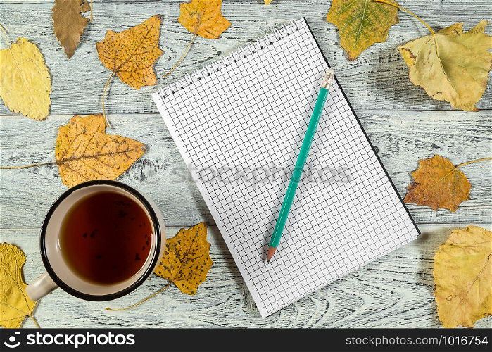 yellow autumn leaves, a Cup of tea and a notebook on a light old wooden background with empty space for text. the view from the top. flat lay